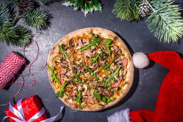 Sfondo decorato di natale con pizza ai peperoni e funghi, consegna e ristorante pranzo di natale e menu per feste, babbo natale consegna la pizza per natale, sfondo di cemento nero vista dall'alto spazio copia