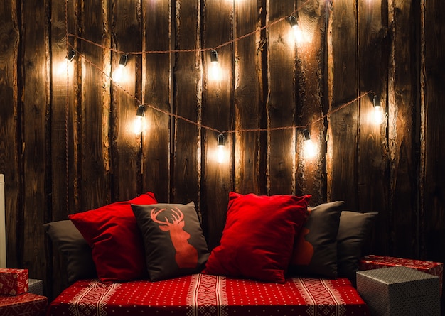 Christmas decorated place in a room with old wooden wall, lamps, red deer pillows and plaid