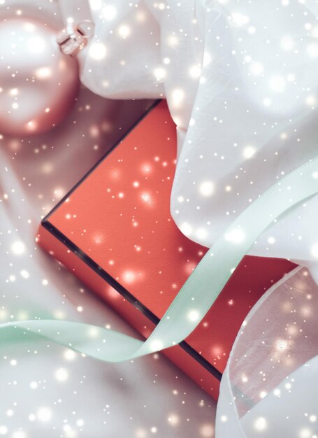 Фото Новогоднее украшение и подарочная коробка с блестящим снегом на шелковом фоне праздничного сезона