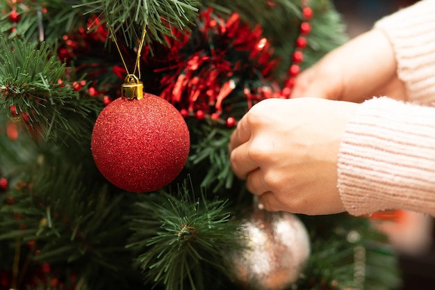 Christmas decoration of a fir female hands hang a ball toy on a green tree