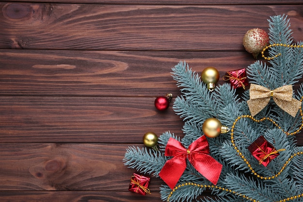 Christmas decoration. Fir-tree branch with balls, gifts and bows on a brown background