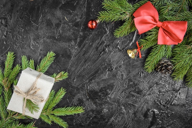 クリスマスの飾り。ボール、ギフト、松ぼっくり、黒い木の表面に弓とモミの木の枝