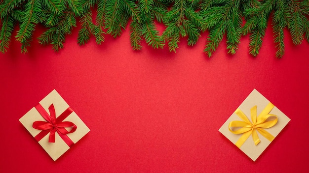 전나무의 크리스마스 장식과 빨간색 종이 배경 상단 보기에 노란색 황금색과 빨간색 리본 활이 있는 포장된 빈티지 선물 상자