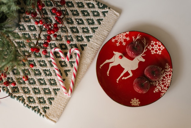 Christmas decoration flat lay. Red deer plate and sugar apples, candy cane and red berries