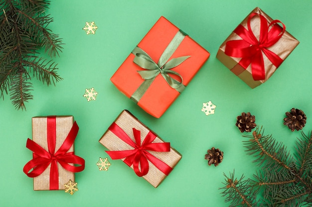 Christmas decoration. Gift boxes, fir tree branches with cones and decorative snowflakes on green background. Top view. Christmas greeting card concept.