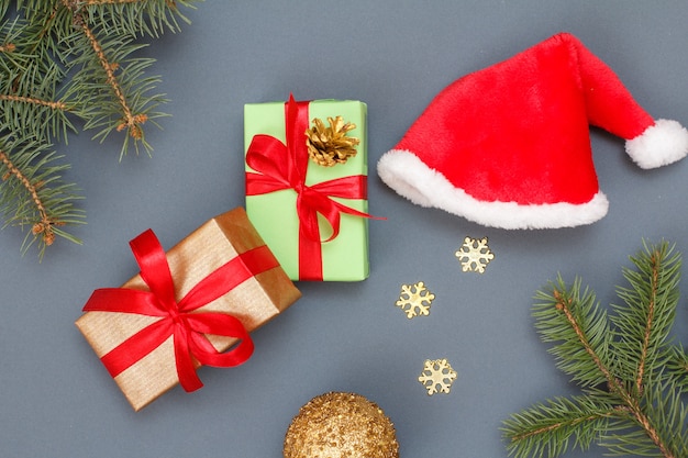 Christmas decoration. Gift boxes, Santa's hat, toy ball, decorative snowflakes and natural fir tree branches on gray background. Top view. Christmas greeting card concept.