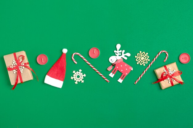 Christmas decoration gift, Santa Claus hat, candy, snowflake on green background. Flat lay