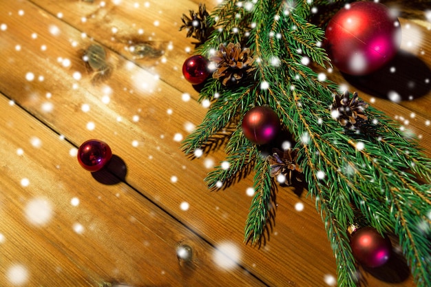рождественские украшения, праздники, новый год и концепция декора - крупный план натуральной еловой ветки, шара и шишки на деревянном столе