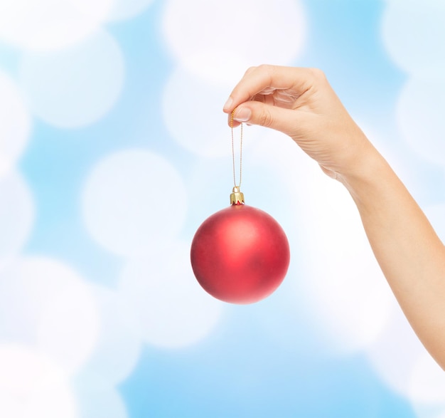 Photo christmas, decoration, holidays and people concept - close up of woman hand holding christmas ball over blue lights background