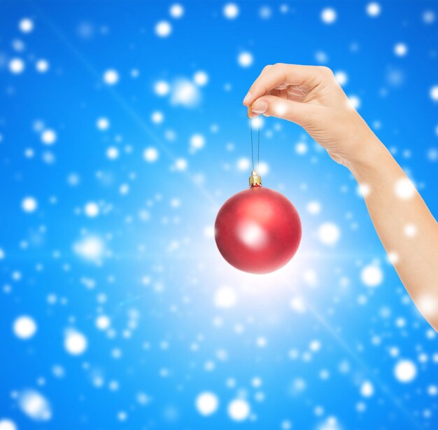 christmas, decoration, holidays and people concept - close up of woman hand holding christmas ball blue snowy background