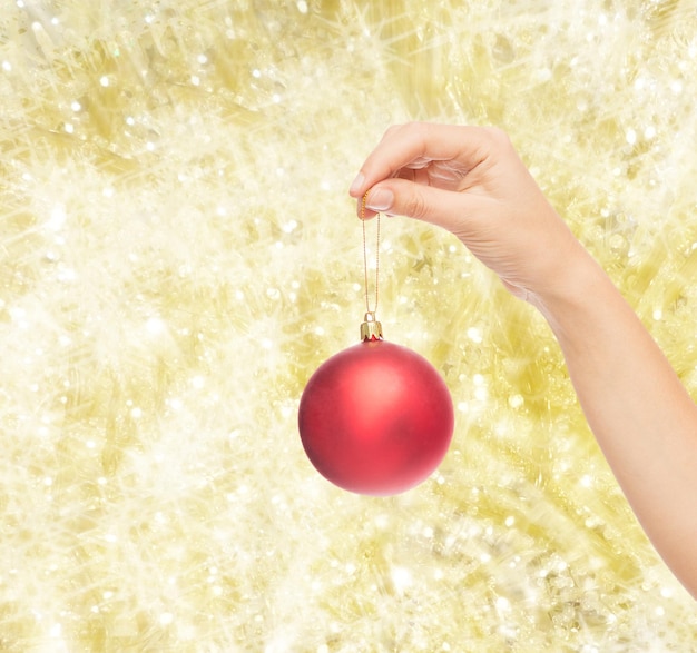 Photo christmas, decoration, holidays and people concept - close up of woman hand holding christmas ball over yellow background