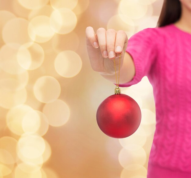 christmas, decoration, holidays and people concept - close up of woman in pink sweater holding christmas ball over beige lights background