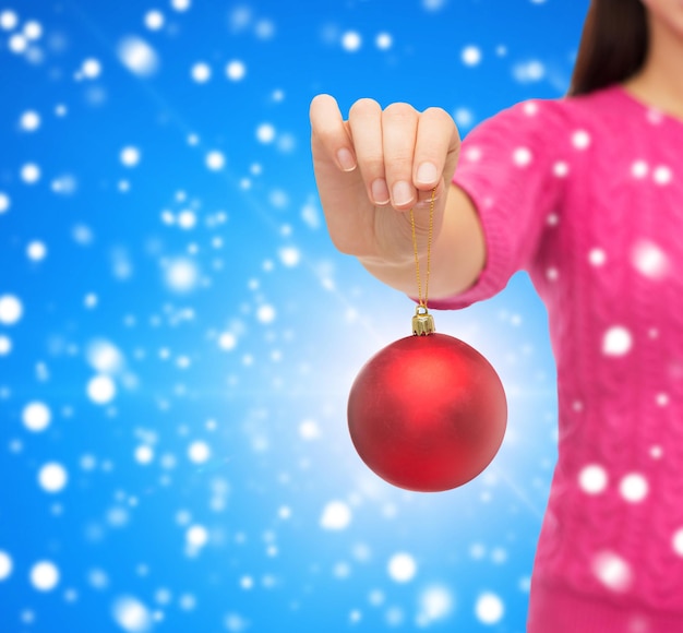 christmas, decoration, holidays and people concept - close up of woman in pink sweater holding christmas ball blue snowy background