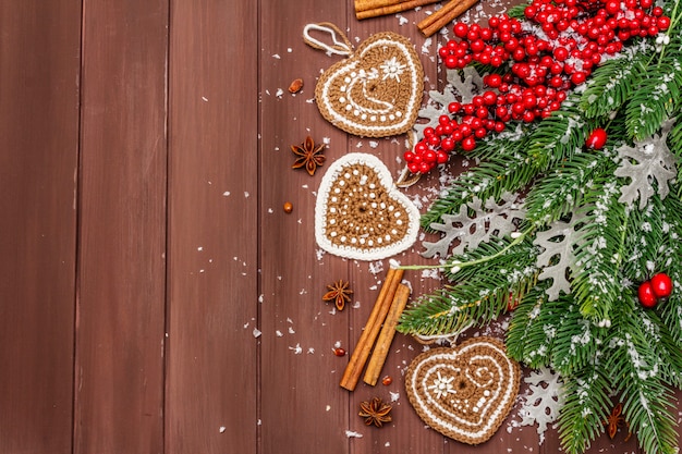 Foto decorazione natalizia. abete di capodanno, foglie fresche, cuori di biscotti allo zenzero all'uncinetto, spezie e neve artificiale.