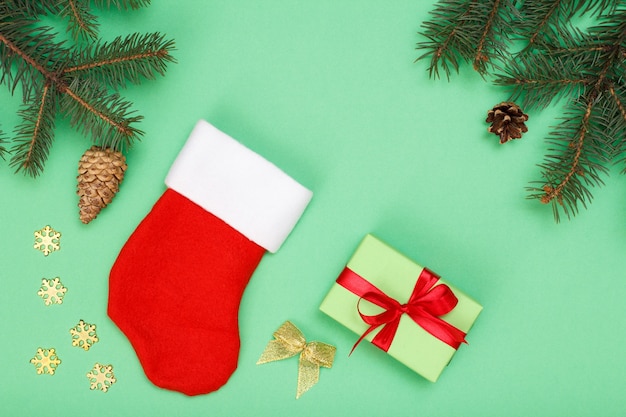 クリスマスの飾り。サンタさんのブーツ、ギフトボックス、緑の背景にコーンとクリスマスのおもちゃとモミの木の枝。上面図。クリスマスのグリーティングカードのコンセプト。