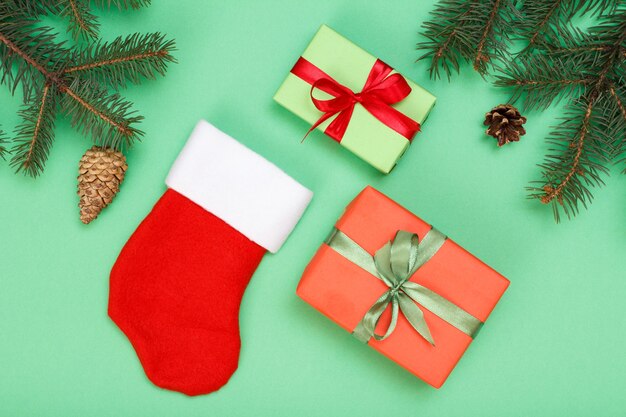 Christmas decoration. Santa's boot, gift boxes, fir tree branches with cones and christmas toys on green background. Top view. Christmas greeting card concept.