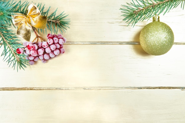 Christmas decoration, a spruce branch with red berries and a yellow bow and another Christmas branch with a Golden ball on a Golden wooden table