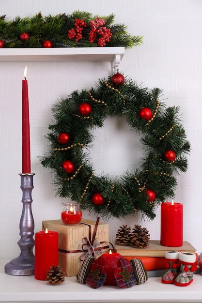 Christmas decoration with wreath, candles and present boxes on shelf on white wall surface