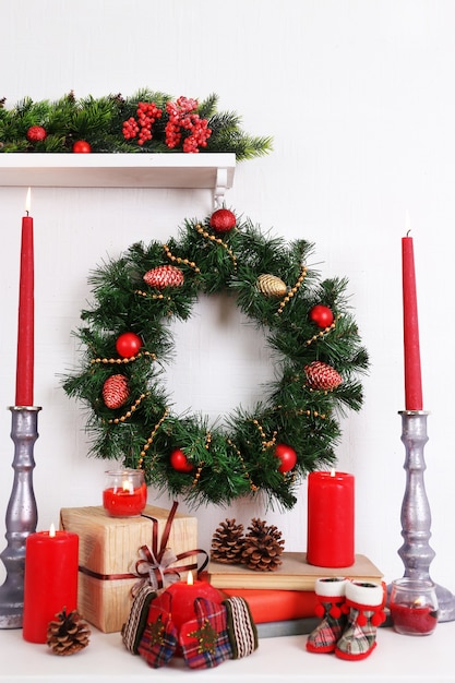 Christmas decoration with wreath, candles and present boxes on shelf on white wall surface