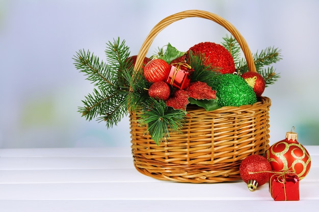 Christmas decorations in basket and spruce branches on table on bright background