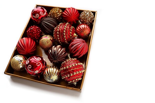 Christmas decorations in a box on a white background Beautiful red and gold balls with sparkles and stripes Preparing for the New Year Christmas holidays Beautiful decorations Copy space isolated