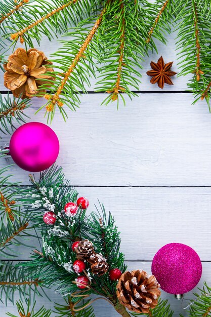 クリスマスの飾り。モミの枝、松ぼっくり、ピンクのボールとクリスマスの装飾的な背景の境界線。トウヒの枝とクリスマスの木製の背景。スペースをコピーします。フラットレイ