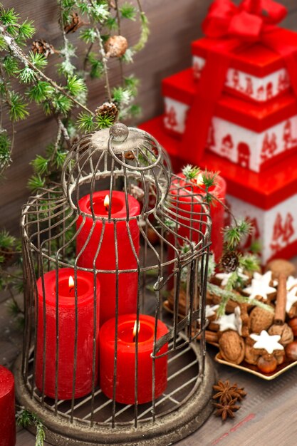 Decorazioni natalizie, confezione regalo, candele rosse, biscotti, noci e spezie su fondo di legno. interni di casa in stile vintage con rami di pino