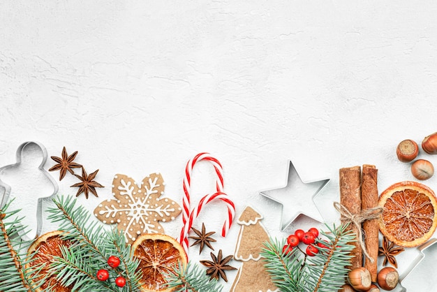 Christmas decorations, gingerbread cookies, candy cane, cookie cutters, nuts, oranges, anise, berries and sprigs of spruce on a light background