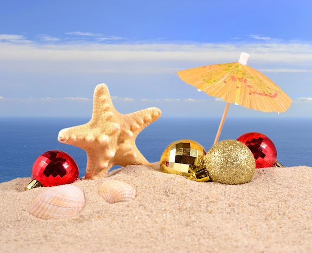 Рождественские украшения, ракушки и морские звезды на песчаном пляже на фоне моря