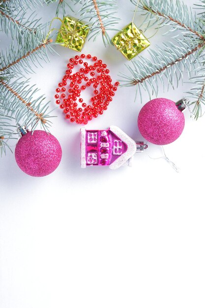 Christmas decorations Spruce branches and holiday decorations on white background Pink balls and toy house Red necklace and golden boxes for festive Christmas tree