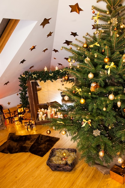 Christmas decorations in the studio, big natural fir tree with golden balls, bows and snowflakes, wooden fireplace and candles 