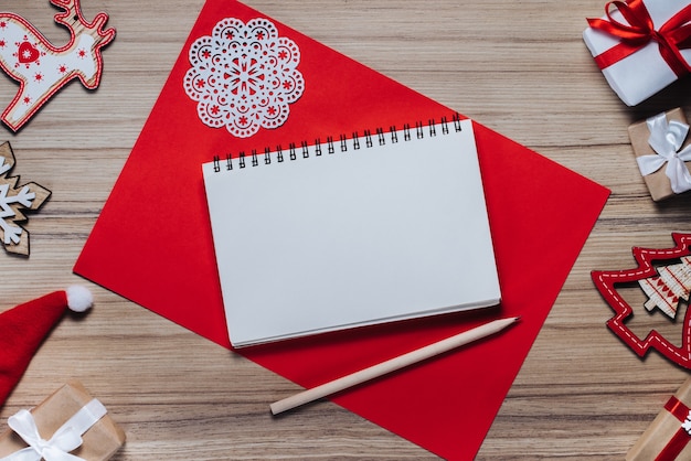 Foto decorazioni natalizie, giocattoli e scatole regalo sulla tavola di legno. taccuino in bianco con una matita per scrivere i migliori auguri.