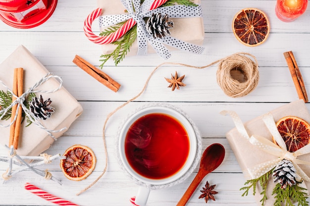 Photo christmas decorations with gift boxes, pine cones and cup of tea on a white wooden background