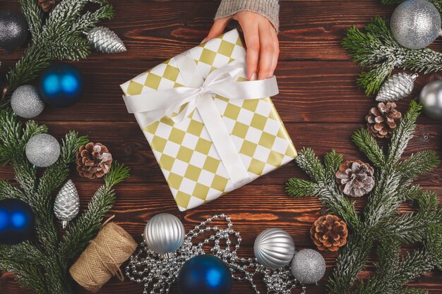 Christmas decorations on wooden table with decorated gift in womans hands