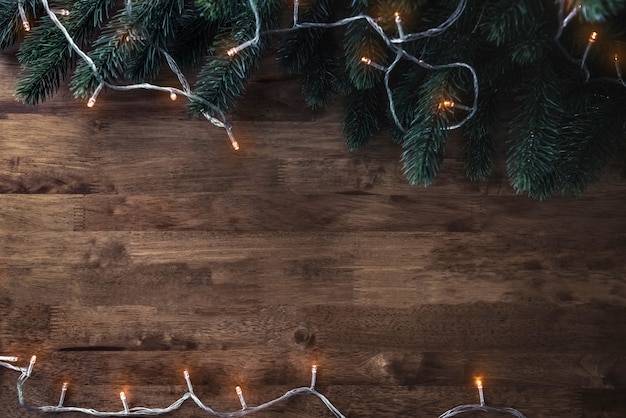 Christmas decorative light with green pine leaves on wood table background