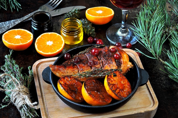Christmas dinner. Chicken breast baked with tangerines and cranberries. Christmas tree branches and a glass of wine.