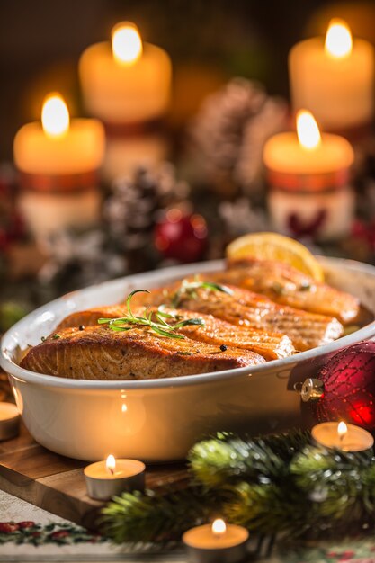 お祝いの装飾のアドベントリースと燃えるろうそくを添えたロースト皿の魚鮭からのクリスマスディナー。