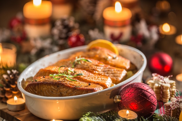 Foto cena di natale a base di salmone di pesce in una teglia con decorazione festiva corona dell'avvento e candele accese.