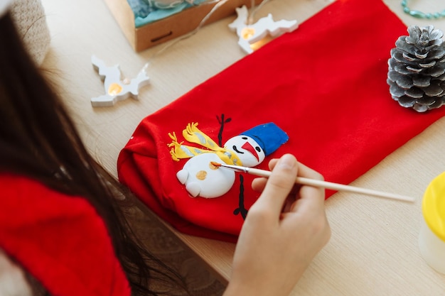christmas DIY childrens hands paint a snowman on a red bag close up