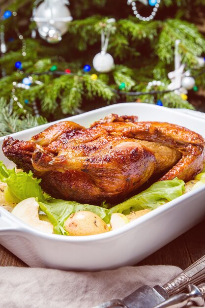 Anatra di natale con mele ed erbe aromatiche in padella bianca con decorazioni di vacanze invernali