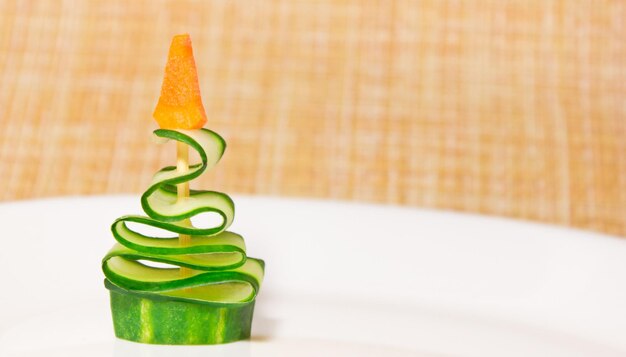 Christmas edible tree made from cucumber and carrot stay on plate. Idea for kids. New Year food art concept. Copy space. High quality photo
