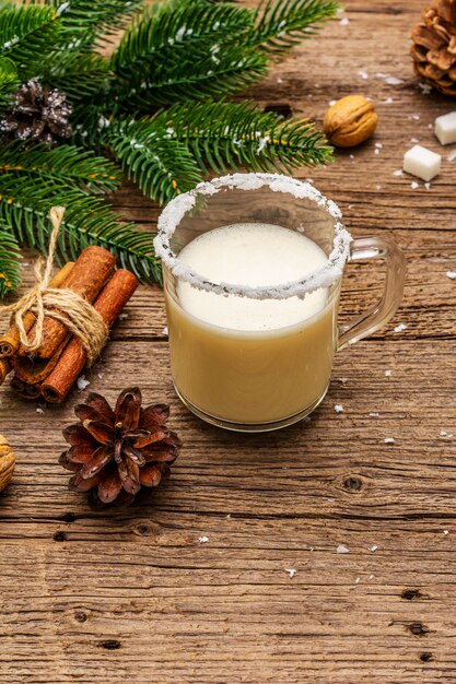 Christmas eggnog liqueur or cola de mono cocktail. Classical winter drink in glass mug, xmas decorations. Evergreen branches, cinnamon, walnuts, sugar.