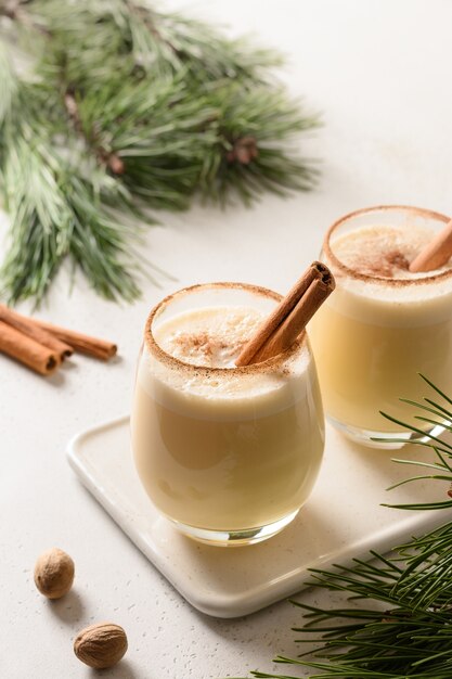 Christmas eggnog with cinnamon on white table decorated evergreen branches.