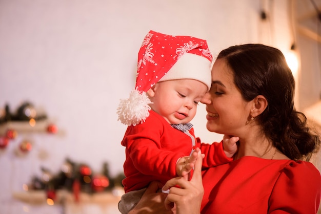 Foto vigilia di natale. famiglia madre e bambino nel gioco di cappelli di babbo natale a casa vicino al camino.