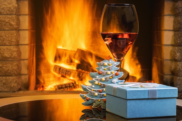 Christmas eve gift box and a glass of wine near cozy fireplace in country house