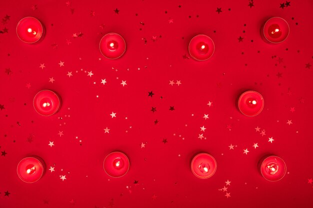 Sera di natale o composizione di san valentino a base di candele accese, glitter sulla superficie rossa. buon natale e felice anno nuovo, felice concetto di san valentino.