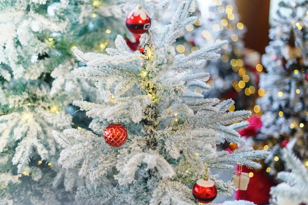 Christmas fairy light on white snow tree, red balls fir tree toys. Blurred background.