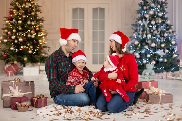 Christmas family Happy mom,dad and little daughter and son on Santa Claus hat. Enjoying love hugs, holidays people. Christmas tree with garlands in decorated room background. Togetherness concept