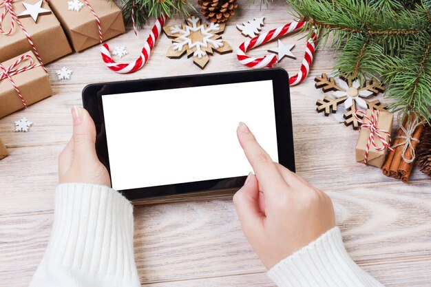 Christmas of female hands uses opened tablet  on rustic wooden table covered with Christmas decoration, top view, flat lay