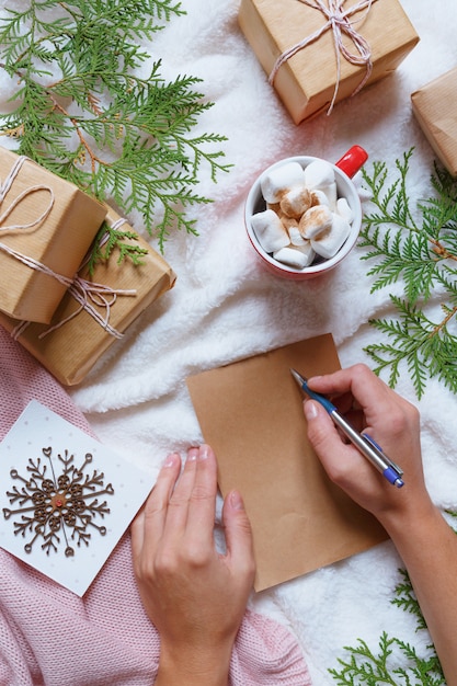 クリスマスの祝祭居心地の良い配置、女性の手はサンタに手紙を書く、お祝いの箱、